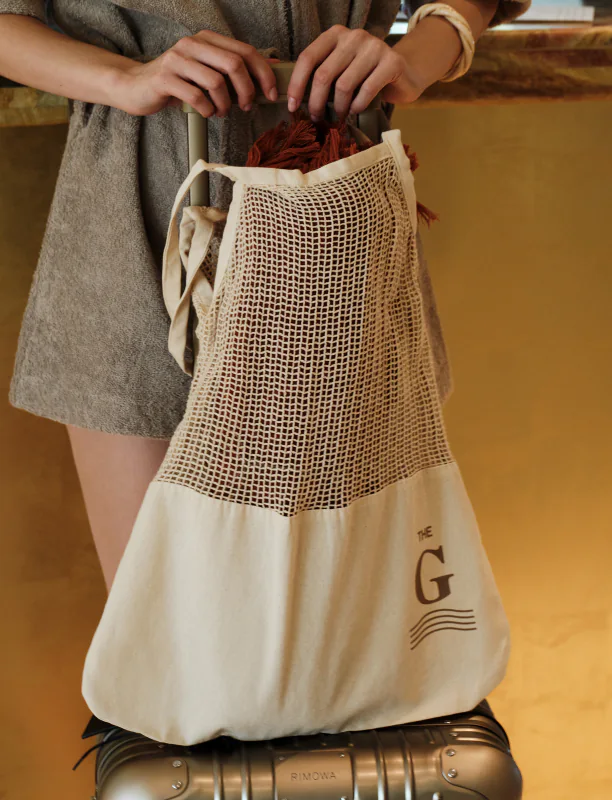 A guest checking out of a hotel, holding a branded goodbye gift bag along with their suitcase.