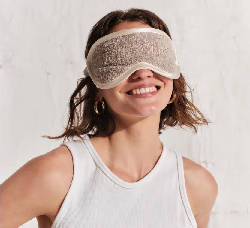 Smiling woman wearing a embroidered sleep mask, a premium hospitality welcome gift.